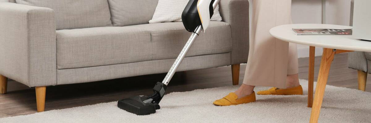 Woman using stick vacuum on carpet.